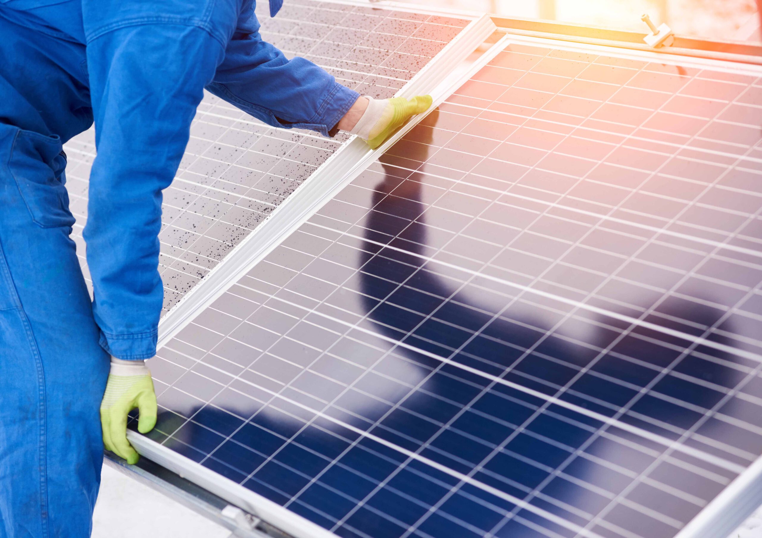 Mann mit Handschuhen positioniert Solarmodul für eine Solaranlage auf einer Dachfläche