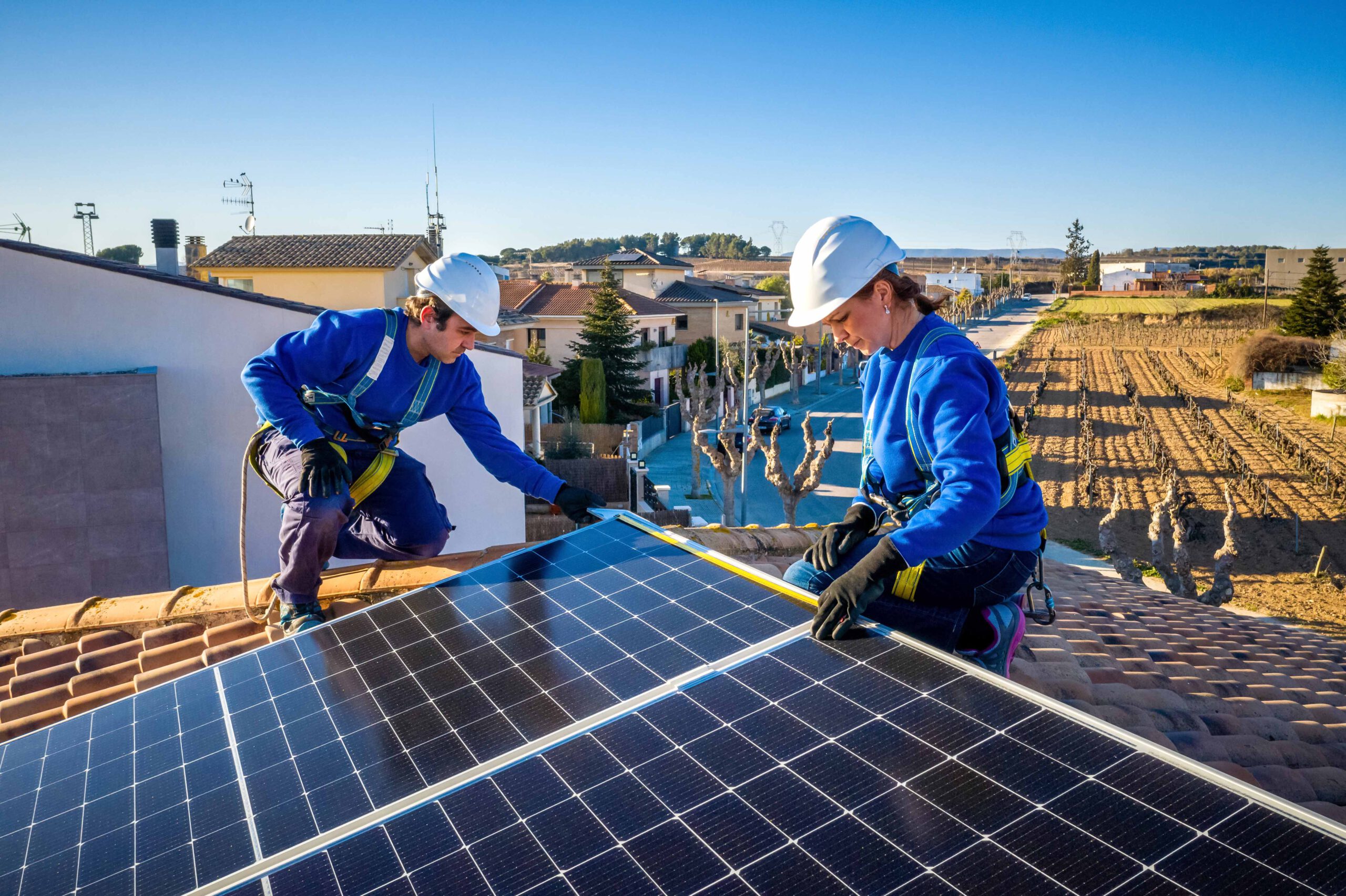 Ein Handwerker und eine Handwerkerin bauen eine Solaranlage auf das Dach eines Wohnhauses