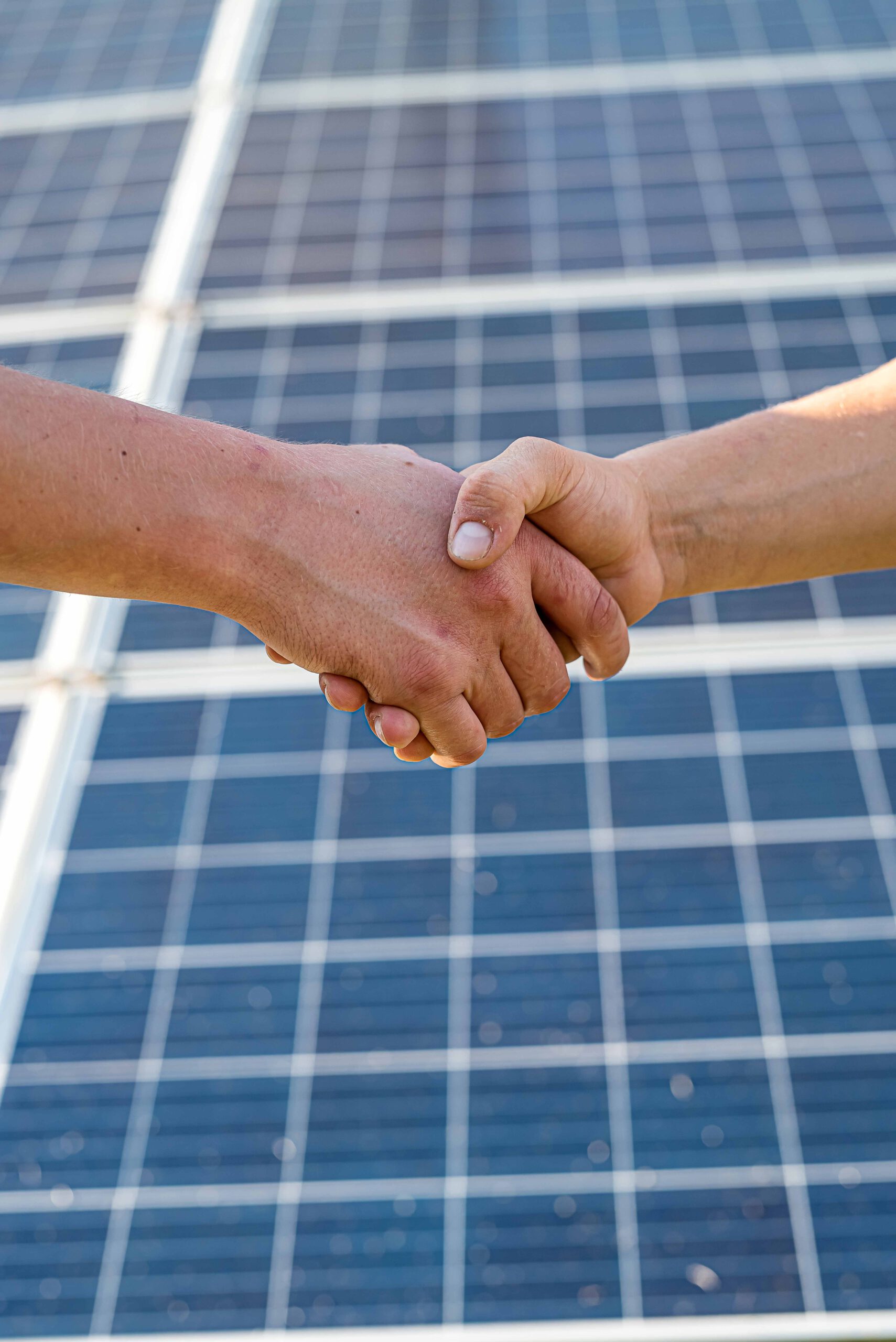 Zwei Hände schütteln einander vor einem großen Solarmodul